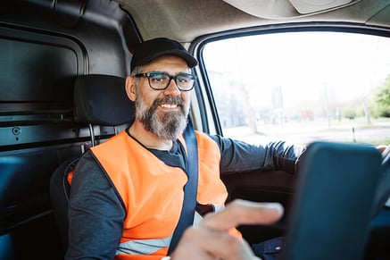 man with service vest, beard, hat and glasses at steering wheel using mobile phone mounted to dash