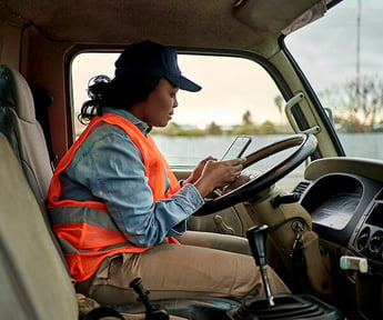 woman in hat and orange service vest at truck steering wheel using phone app