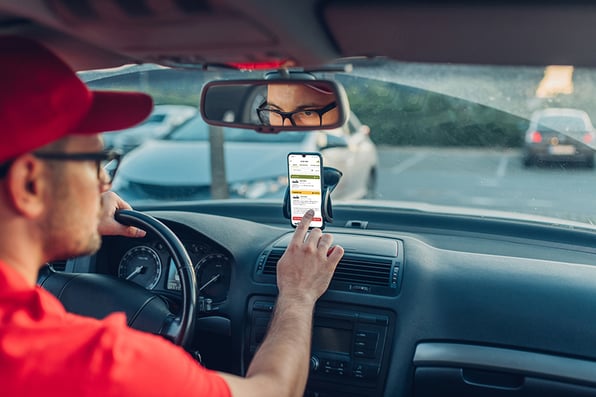 Driver with red hat and shirt using iphone ascend fleet app in vehicle