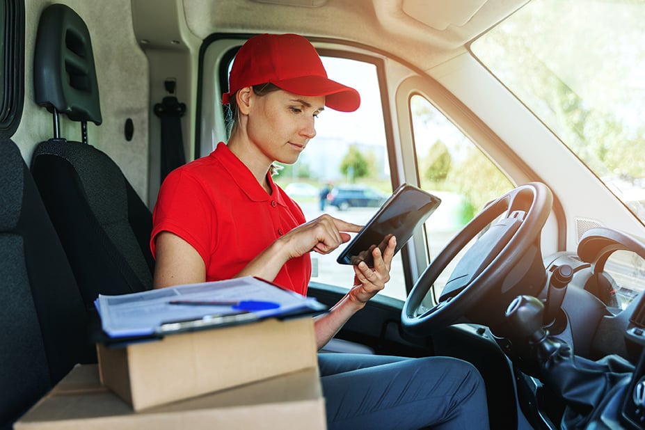 Woman in red hat and shirt at steering wheel using software on tablet